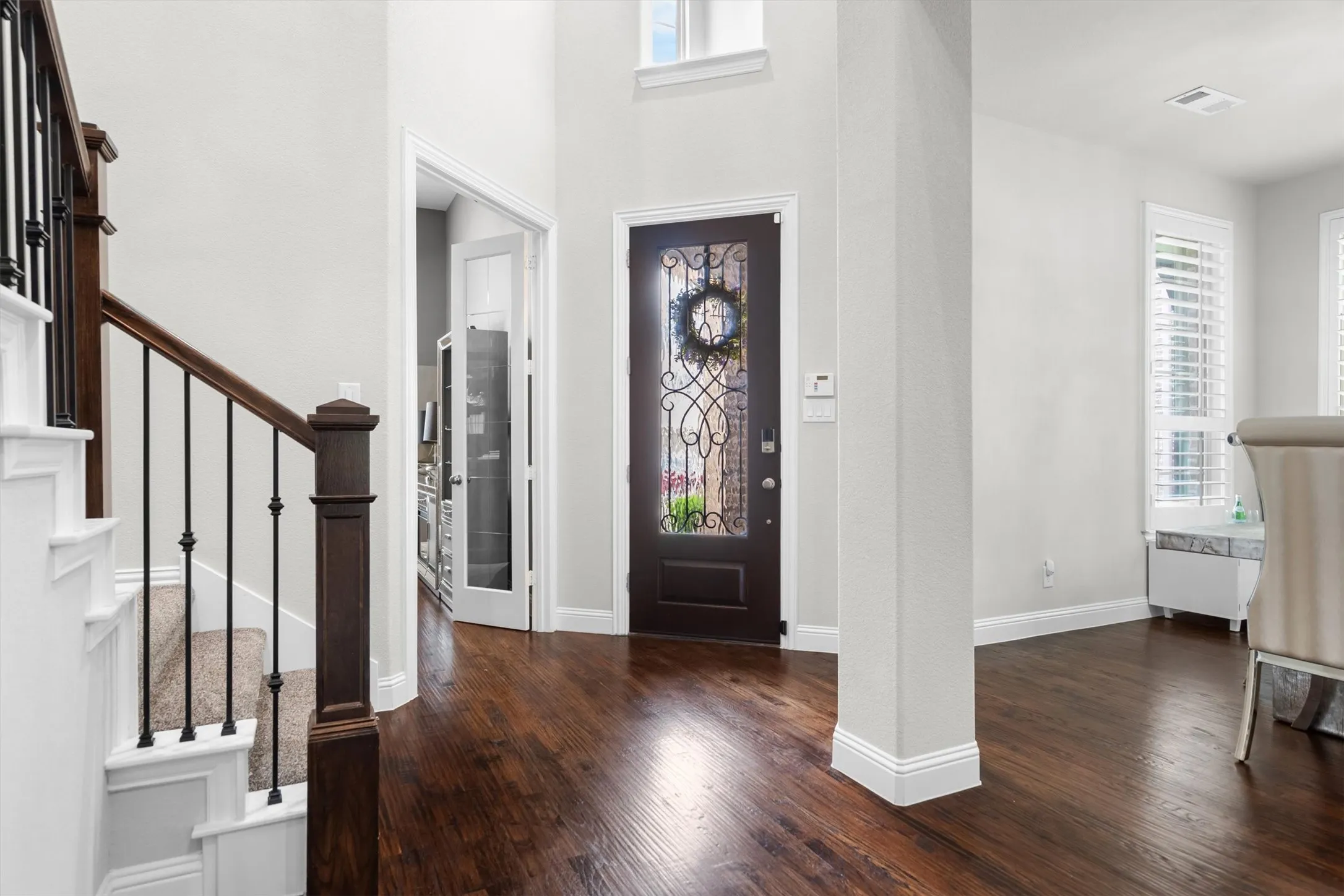 A dramatic wrought-iron staircase and rich hardwood floors greet you at the front door, framed by a decorative glass entry.