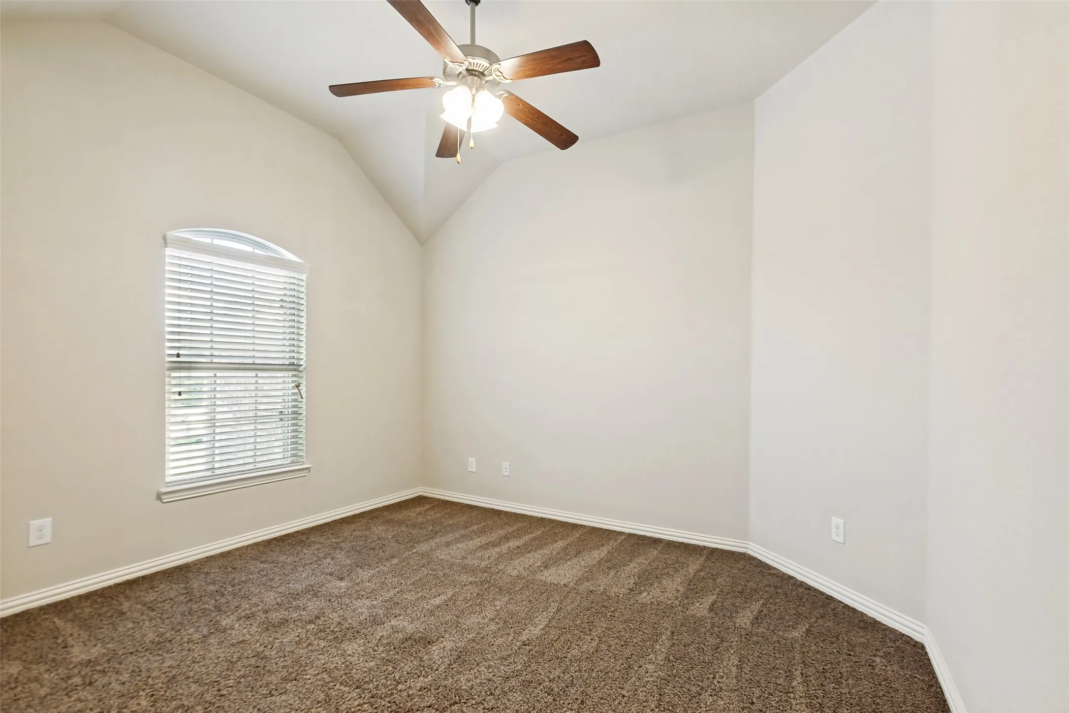 Vaulted ceiling, arched window with blinds, ceiling fan, and carpeted flooring