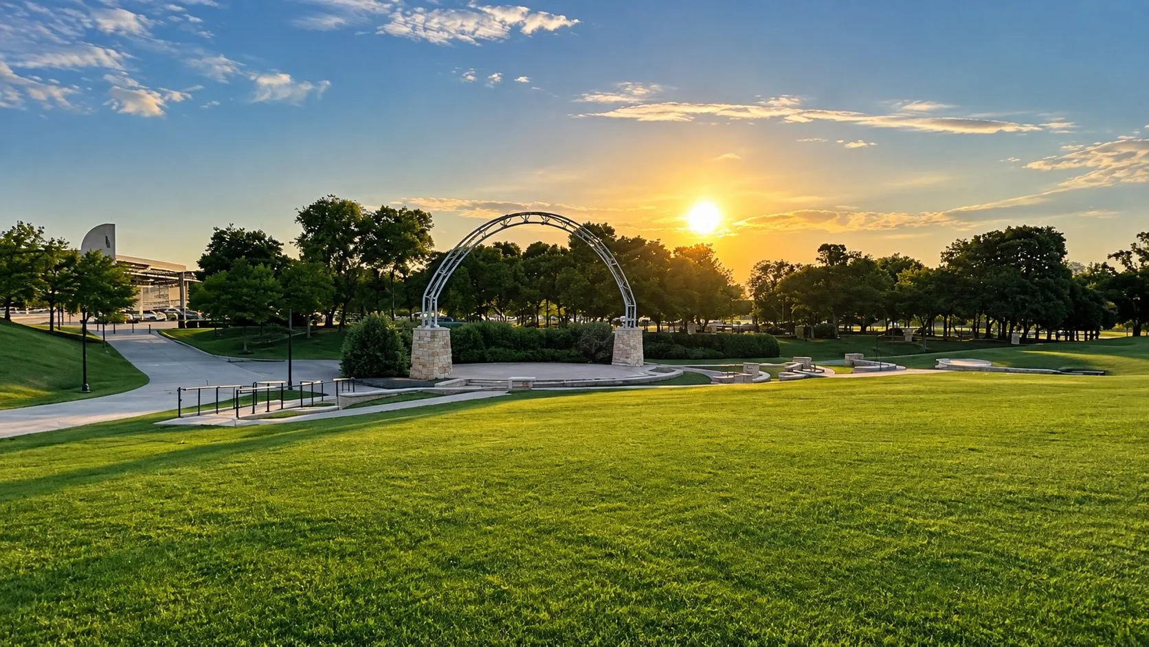 Expansive green space featuring a large grassy lawn, paved walking paths, and mature trees