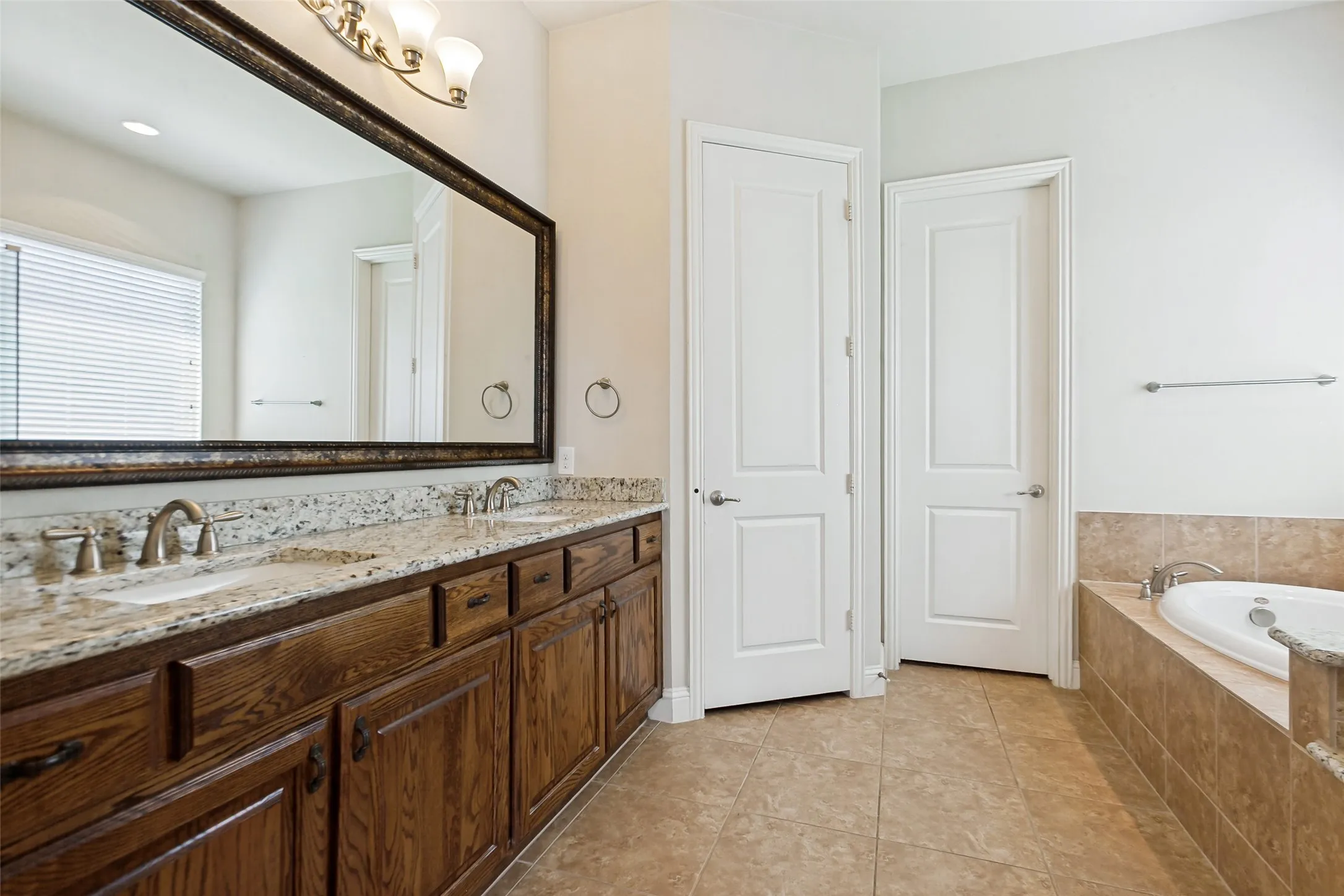 Double vanity with granite countertop, wood-finish cabinetry, and brushed nickel fixtures