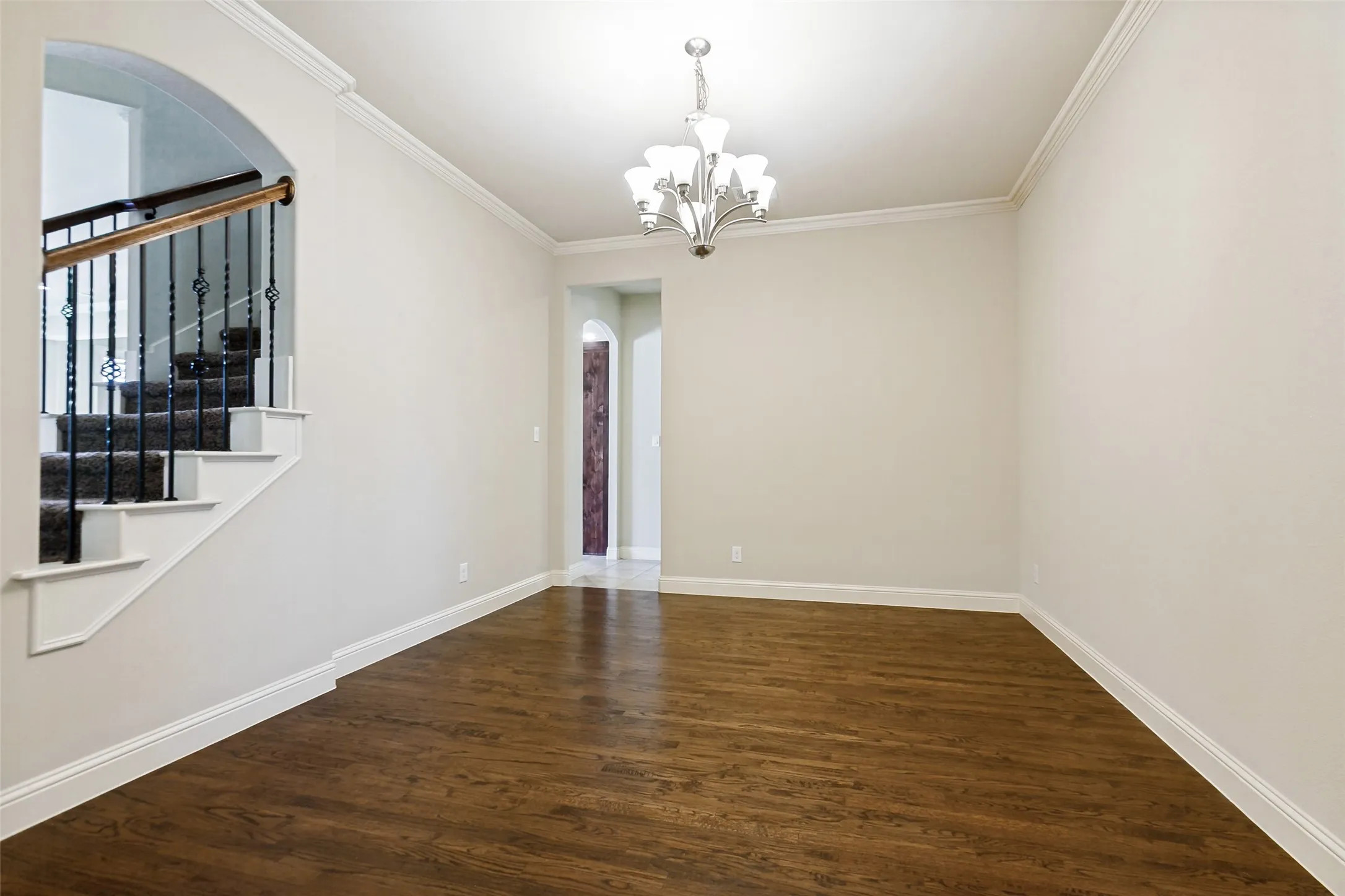 Hardwood flooring, crown molding, arched entryways, and a staircase with wrought iron balusters