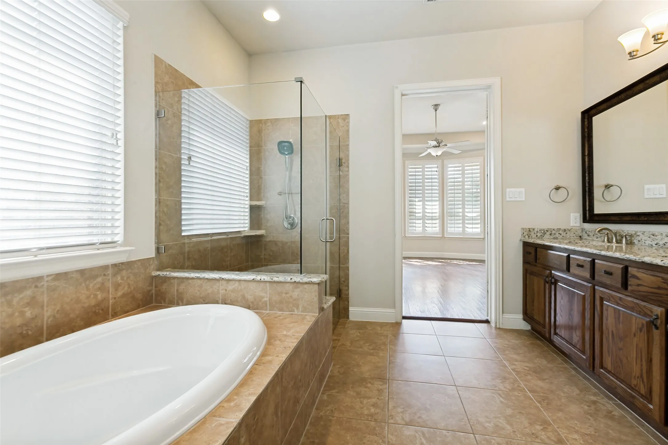 Freestanding soaking tub, walk-in shower with glass enclosure, rich wood-finish vanity with stone countertop, and tile flooring