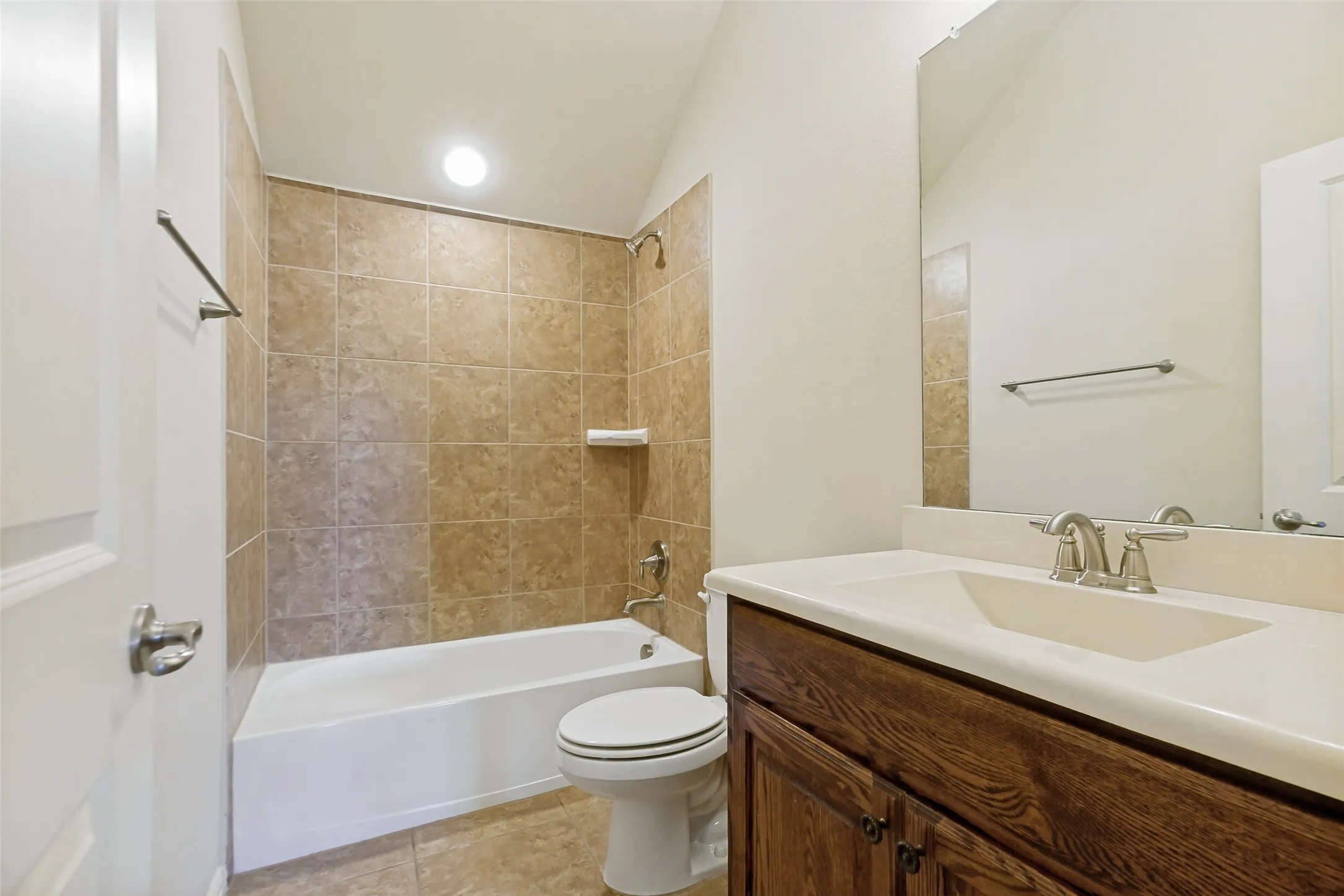 Bathroom featuring a tiled tub shower combination, a single vanity with an integrated sink, a dark wood-finish cabinet, and a wall mirror