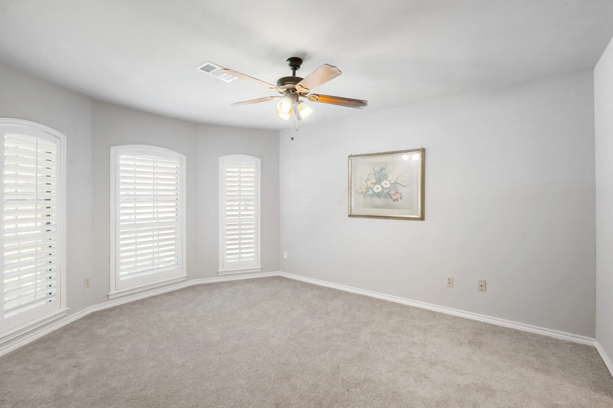 Spacious secondary bedroom featuring plush carpeting, soft neutral tones, and an abundance of natural light through three beautifully framed windows with plantation shutters. The generous layout offers plenty of room for comfortable furnishings and a relaxing retreat.