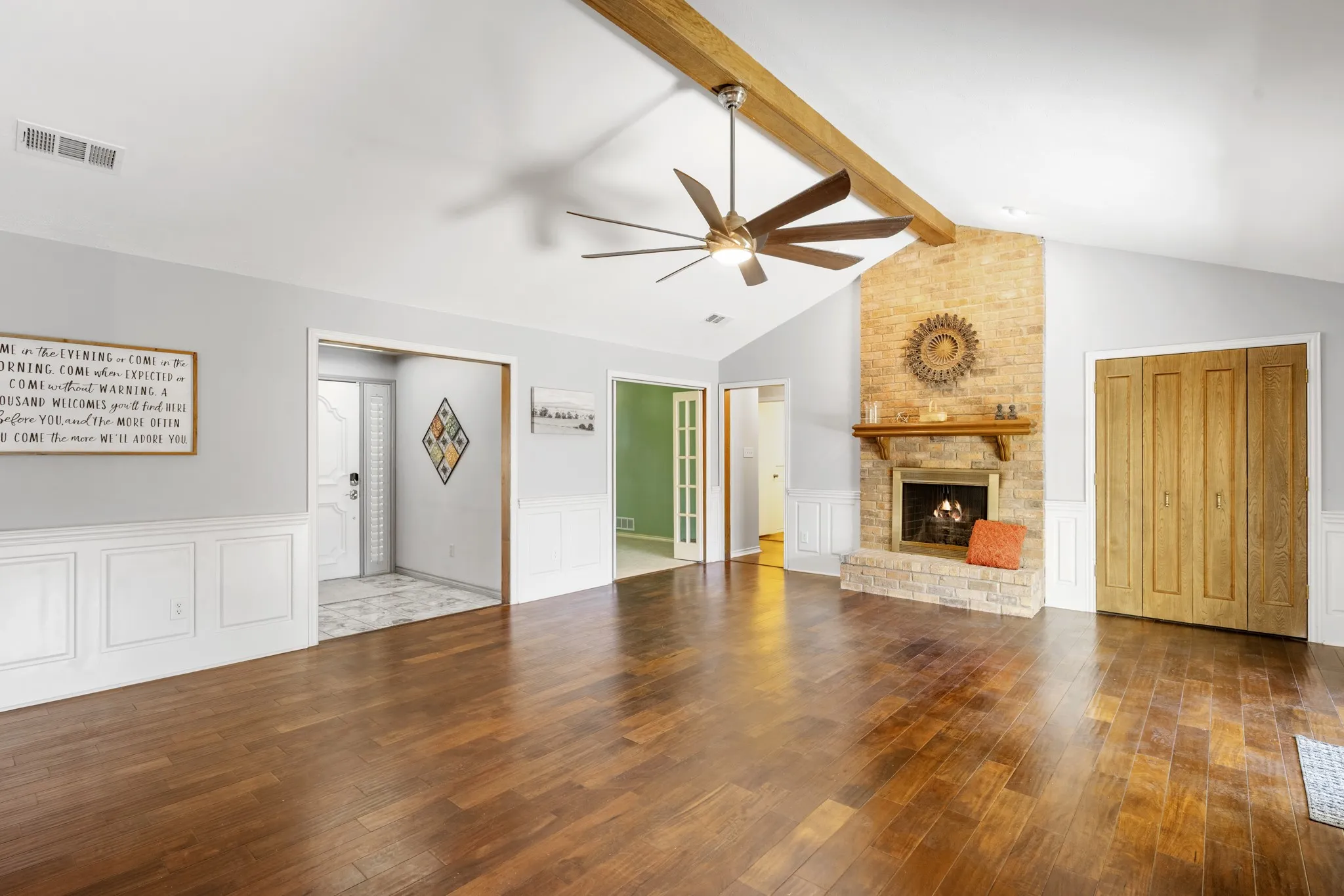 Spacious living room featuring rich wood flooring, and a striking floor-to-ceiling brick fireplace with wood mantel.
