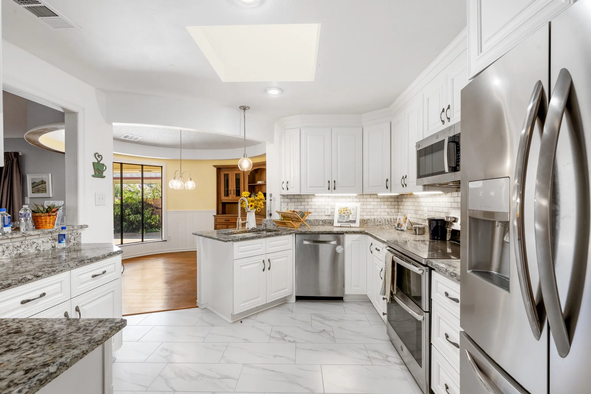 Beautifully updated kitchen featuring crisp white cabinetry, granite countertops, stainless steel appliances, and a stylish subway-tile backsplash. The generous layout offers abundant storage,  and a seamless connection to the bright dining area.