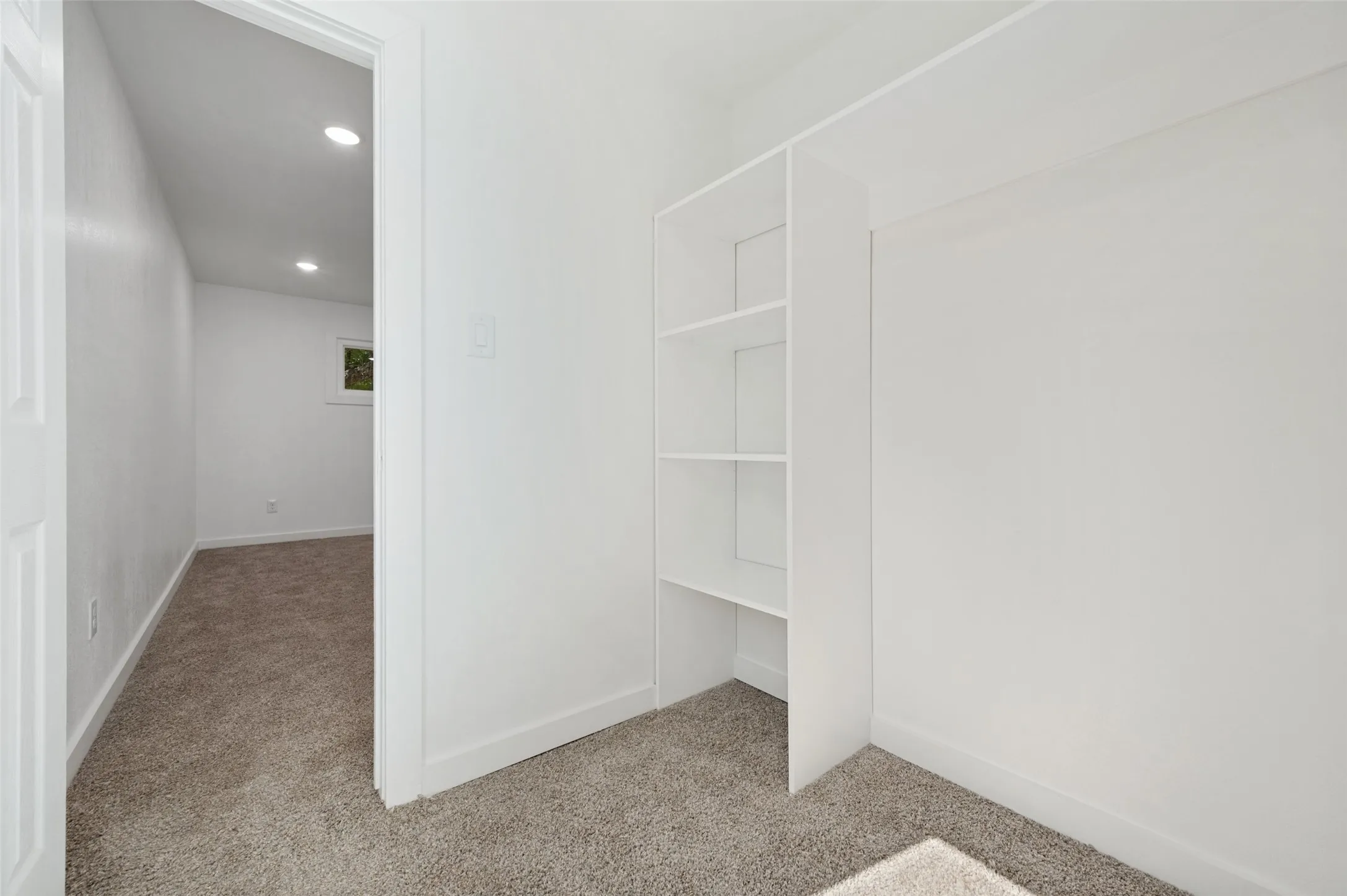 Built-in shelving, recessed ceiling lighting, light-colored carpeting, and a window