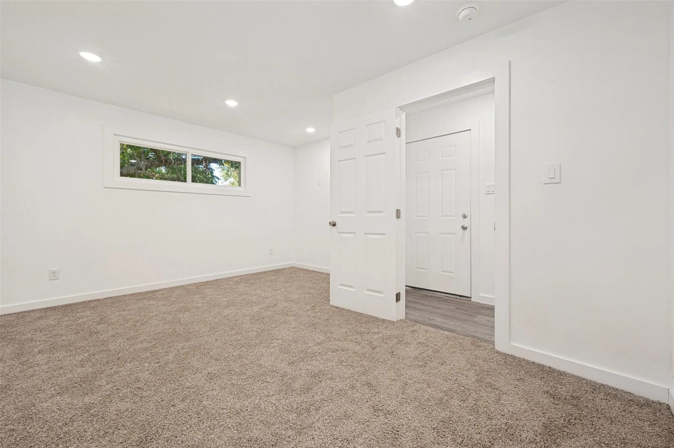 Recessed lighting, neutral tone carpeting, white interior doors, and a window with white trim