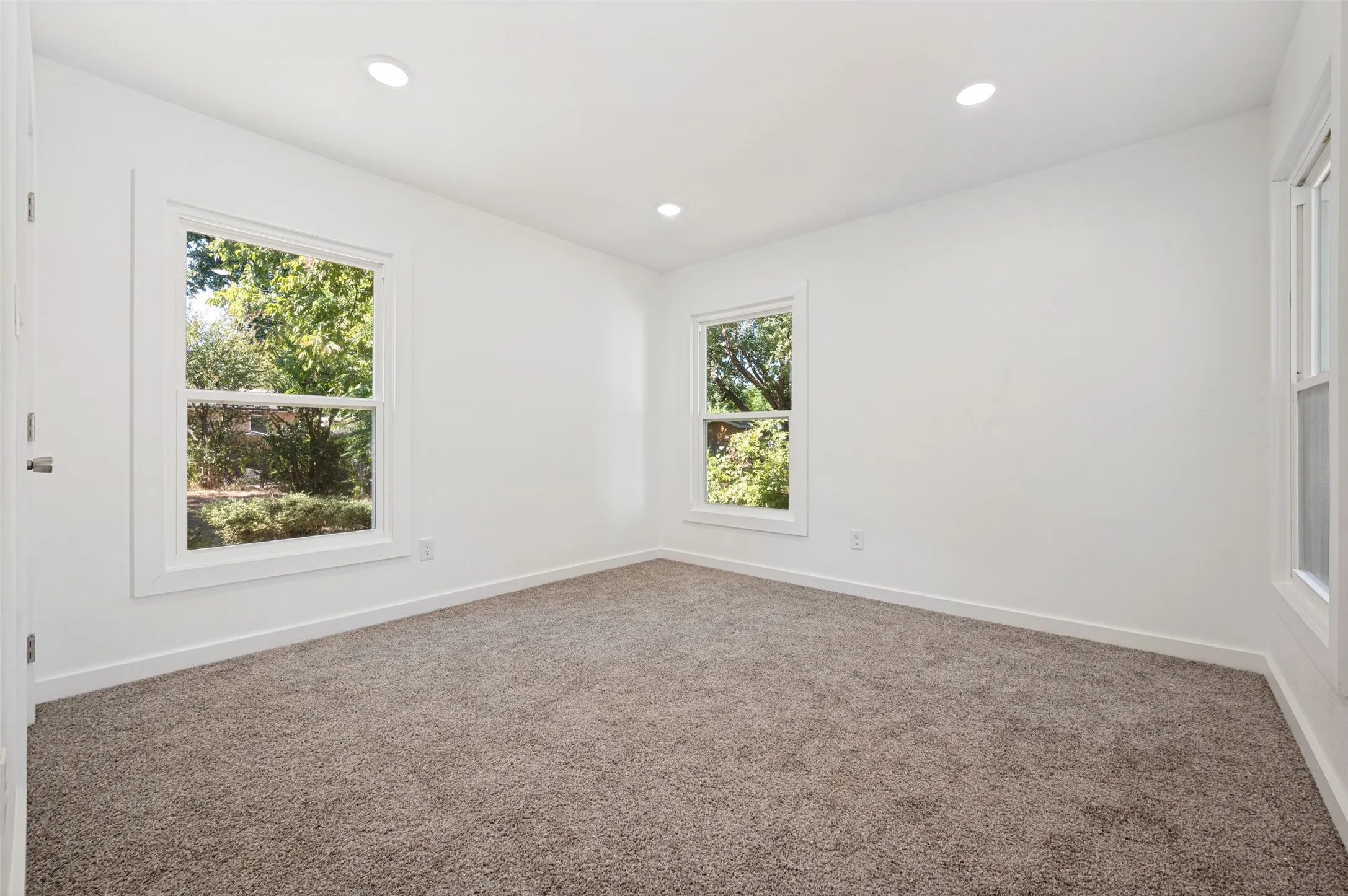 Wall-to-wall carpeting, multiple windows with white trim, recessed ceiling lighting, and a neutral color palette