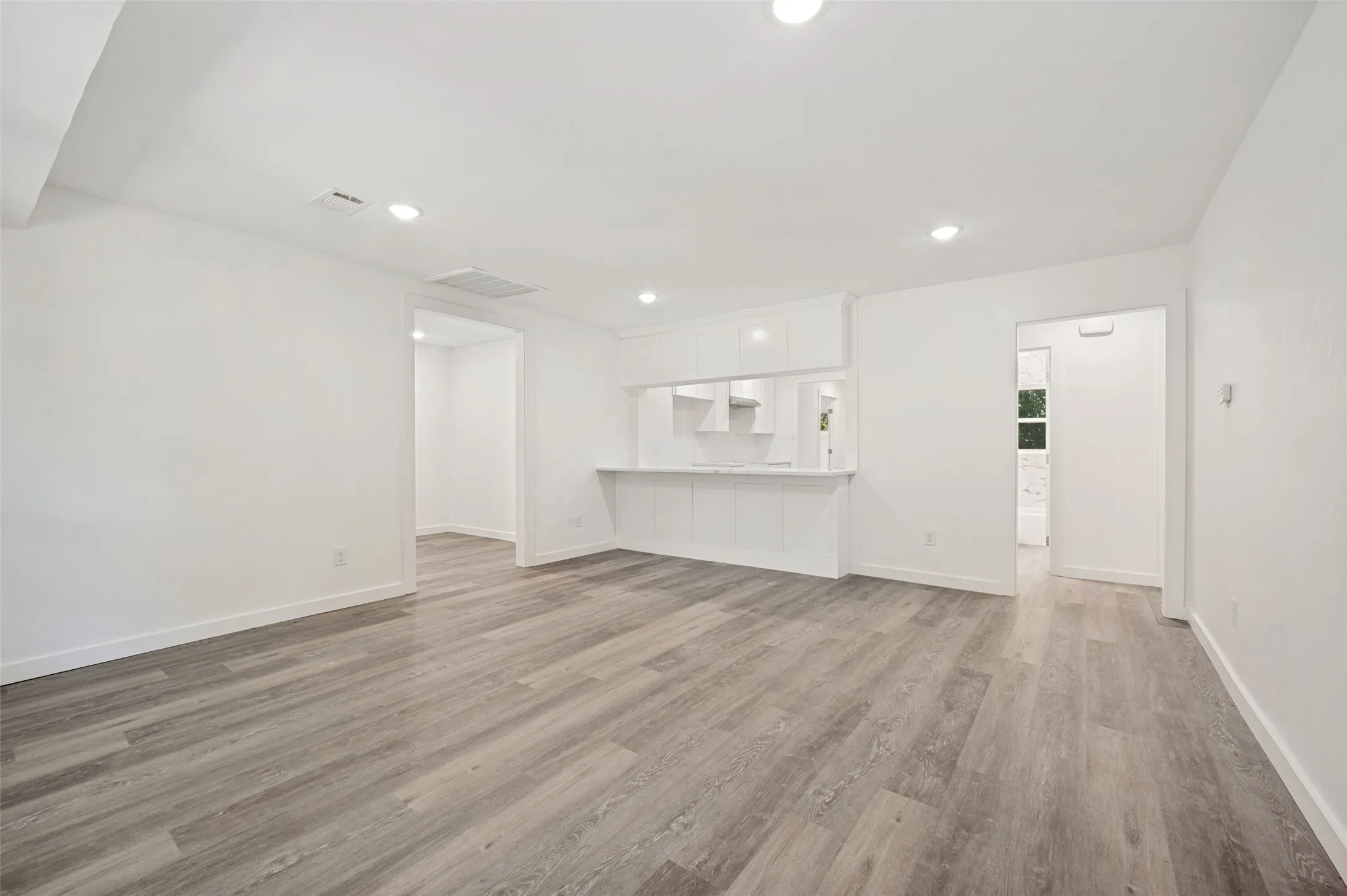 Light wood-finish flooring, recessed lighting, white walls, and a pass-through counter with white cabinetry