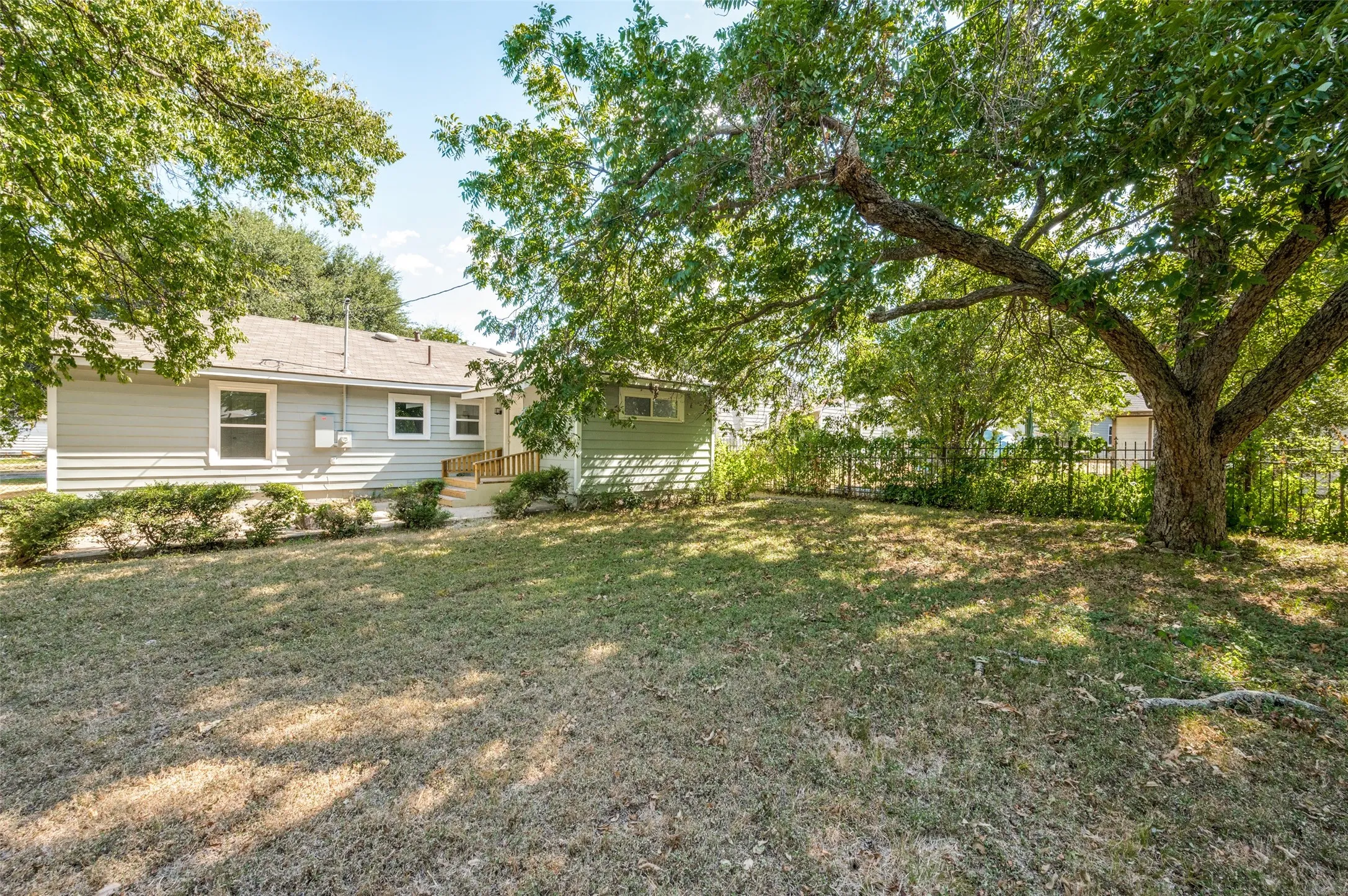 Expansive lawn with mature trees and established landscaping, featuring a fenced perimeter and a house with horizontal siding