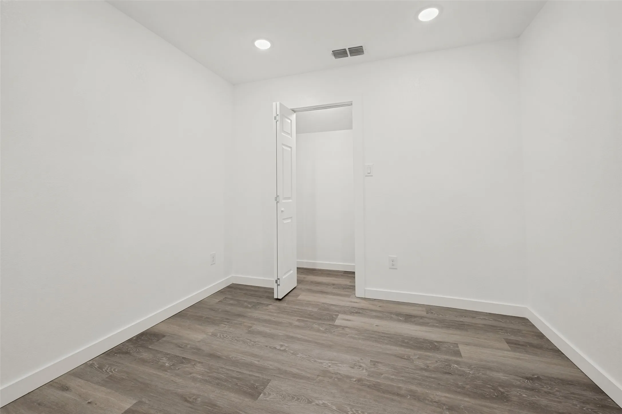 Neutral white wall paint, recessed ceiling lighting, wood-finish flooring, and a bi-fold closet door