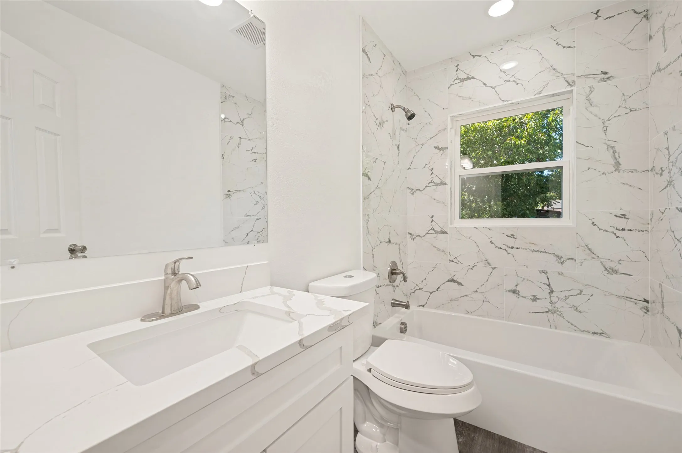 Integrated vanity with a built-in sink, brushed nickel faucet, full-width mirror, tile shower surround, and a soaking tub