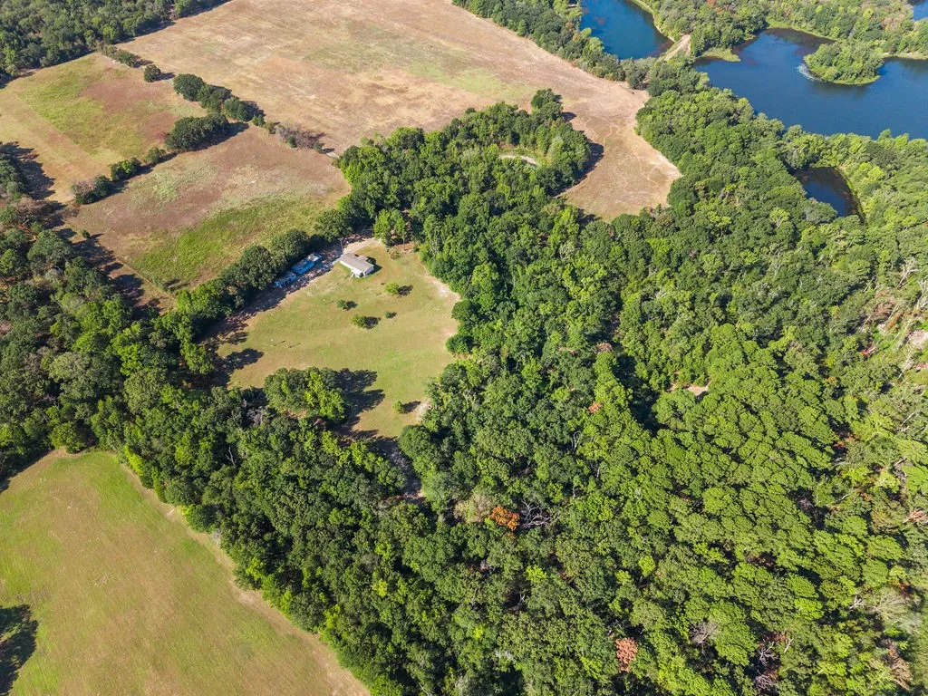 Expansive land parcel featuring open fields, wooded areas, and a visible structure