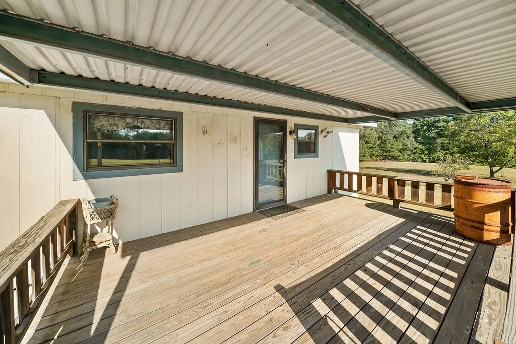 Expansive wooden deck with a corrugated metal overhang, featuring a paneled wood railing and a glass-paneled exterior door