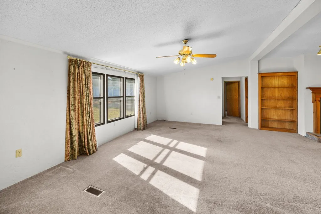 Carpeted living space featuring a window wall, ceiling fan, and built-in wood shelving