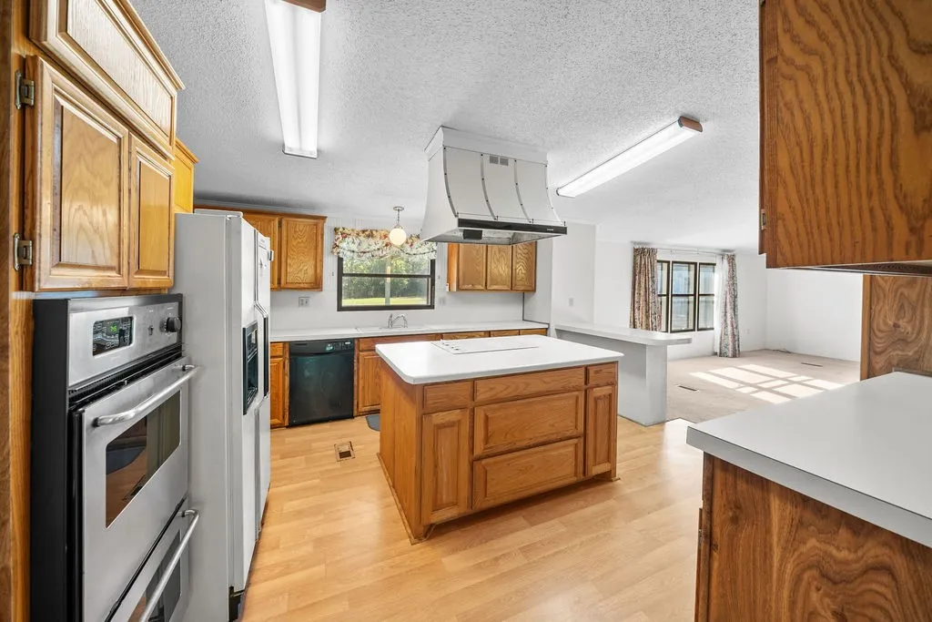 Kitchen featuring wood-finish flooring, wood cabinetry, white countertops, and a center island with a built-in range hood
