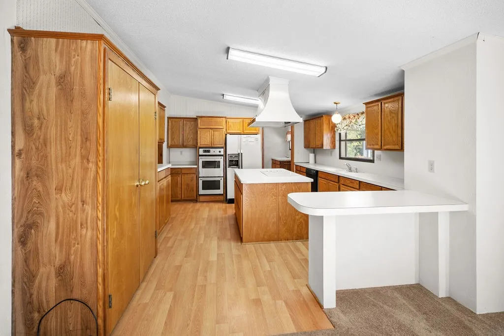 Kitchen featuring wood-finish flooring, a central island with white countertops, built-in double ovens, and a range hood