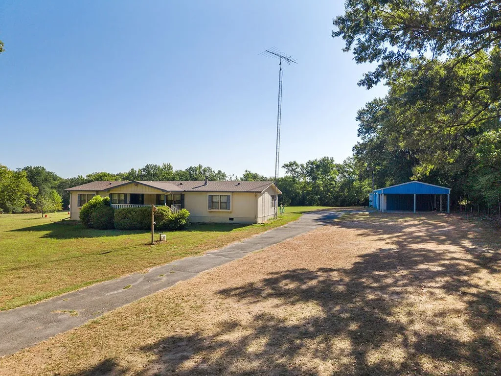 Single-story residence with a covered front porch, an asphalt driveway, and an open-sided blue metal outbuilding