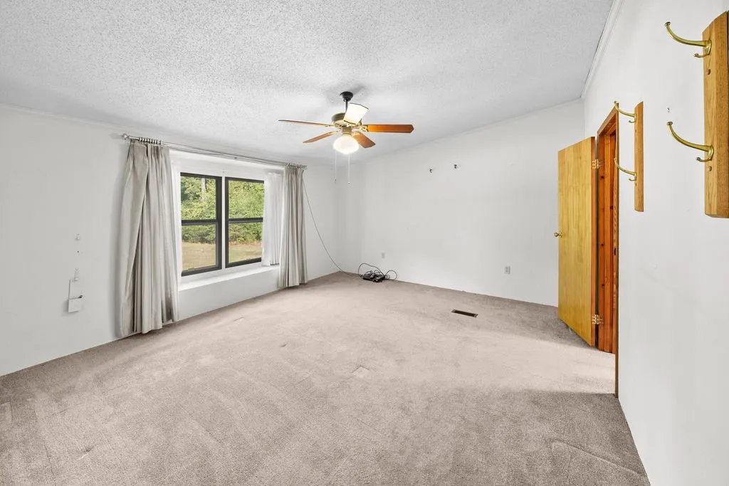Carpeted room featuring a ceiling fan with light fixture, natural light from a window, and a wood-panel door