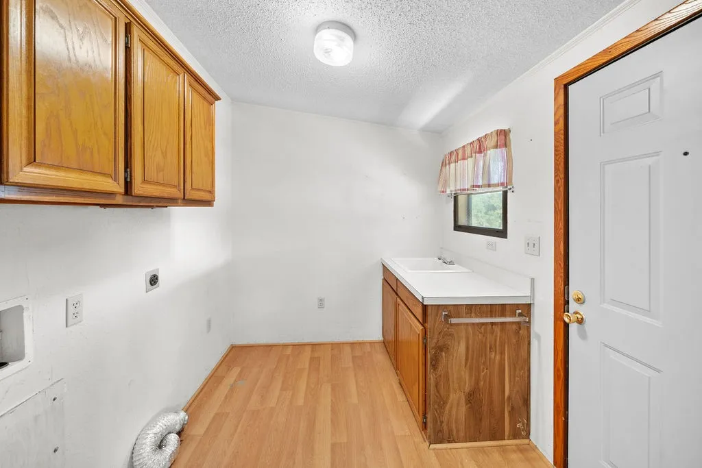 Laundry room with wood-finish flooring, white walls, built-in cabinetry, and a utility sink with a white countertop