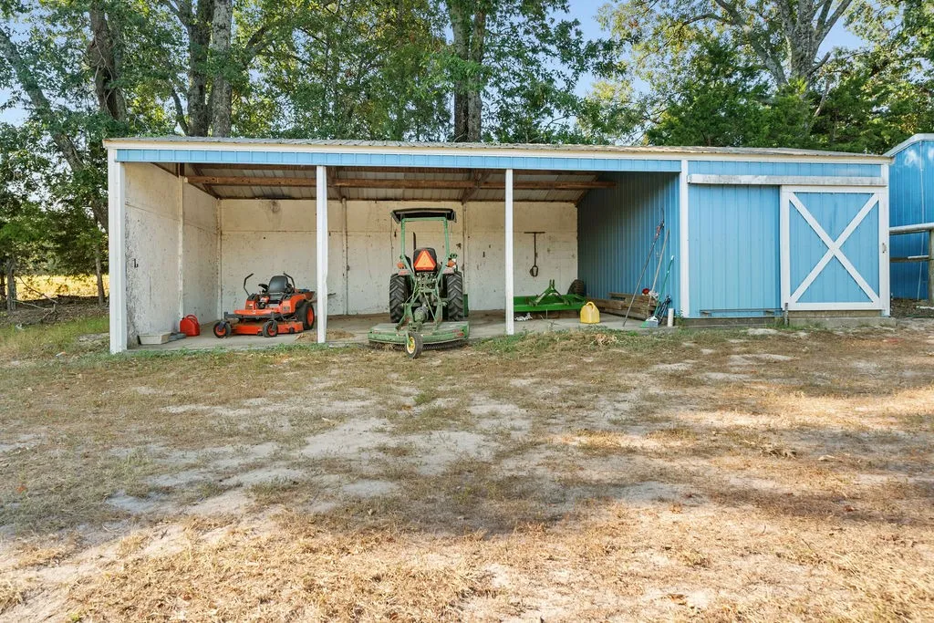 Blue siding utility structure featuring an open-air storage area, covered parking, and an enclosed storage section with a sliding barn door