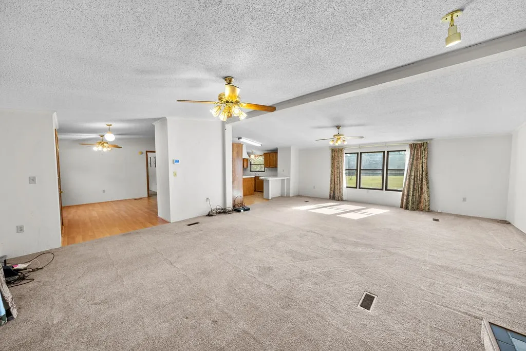 Carpeted living area with multiple windows, ceiling fans, and an open layout to an adjacent room with wood-finish flooring