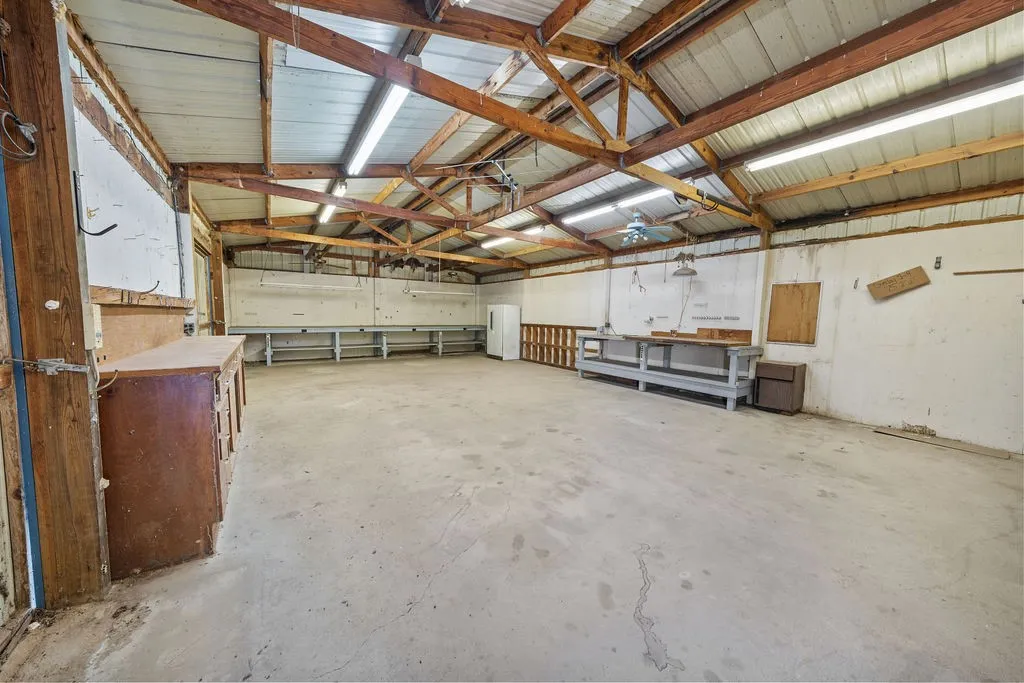 Expansive concrete-floor space featuring exposed wood beam rafters, metal ceiling, and fluorescent lighting