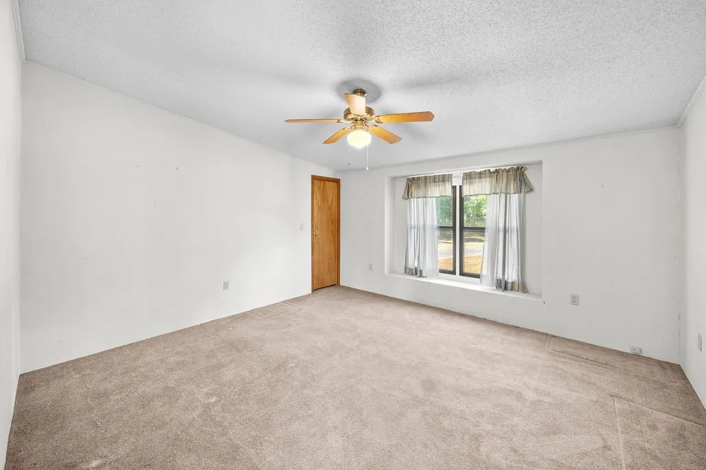 Neutral-toned carpeting, ceiling fan with integrated lighting, and a window with a deep sill