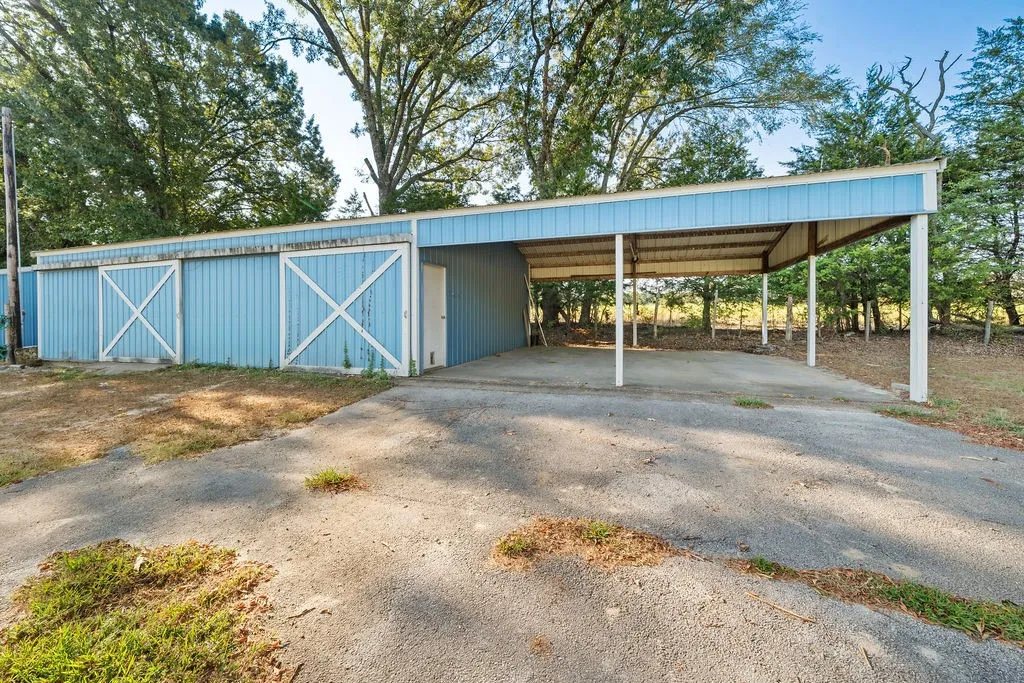 Light blue exterior building with multiple sliding barn doors, an attached carport, and a concrete floor