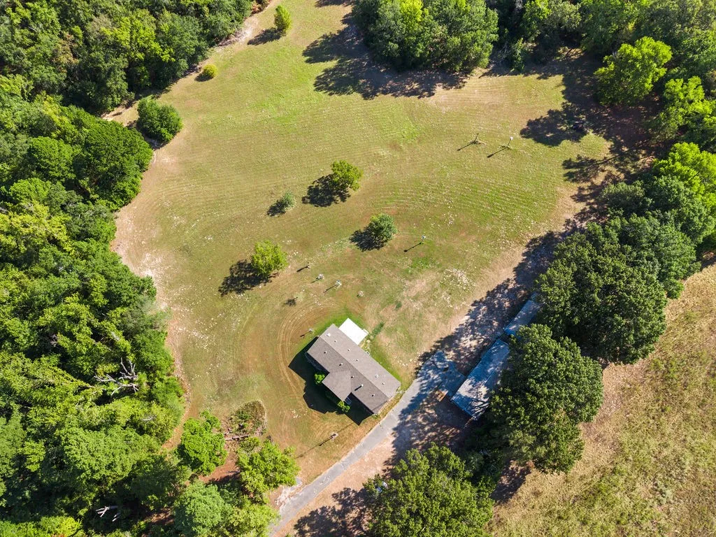 Expansive natural acreage with a perimeter of mature trees, a gravel drive, and a residential structure with a shingle roof