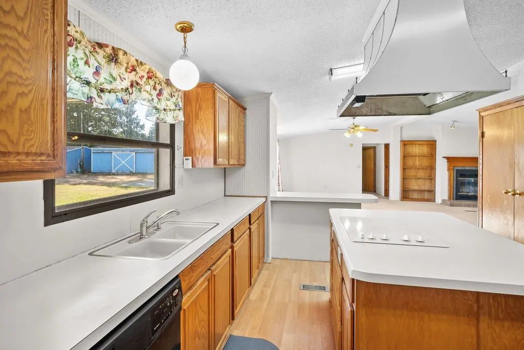 Kitchen featuring wood-finish cabinetry, white countertops, a double basin sink, and a built-in stovetop on the island