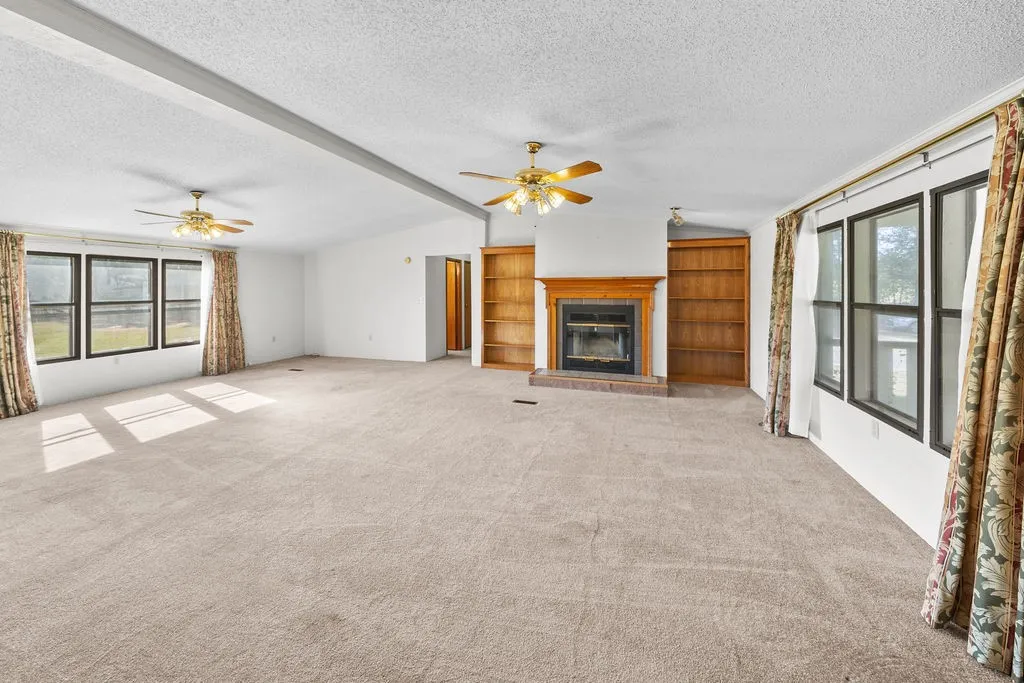 Spacious room featuring a central fireplace with wood mantel, built-in shelving, multiple windows, and two ceiling fans