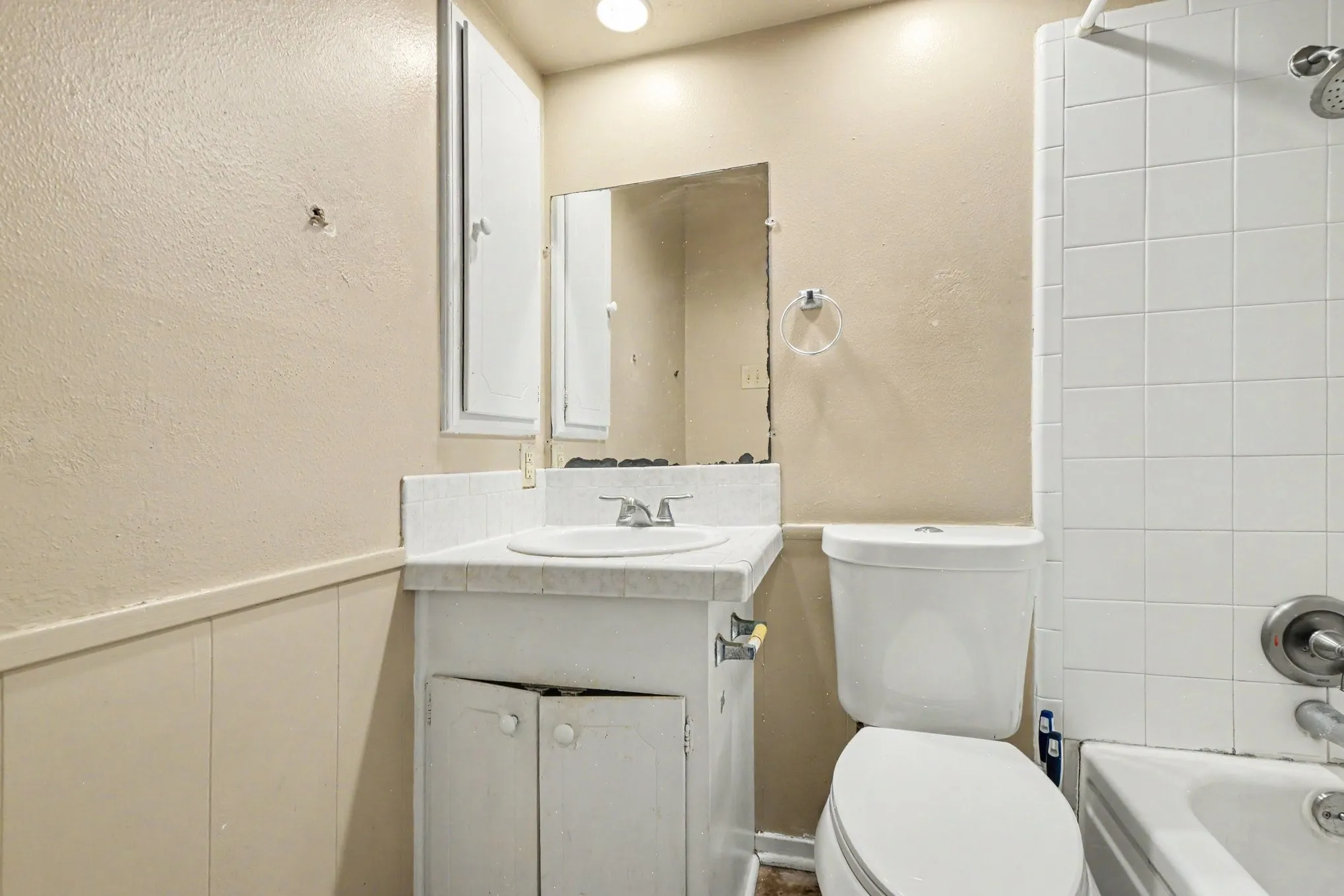 White vanity with an integrated sink and chrome faucet, accompanied by a toilet and a tiled shower-over-tub combination