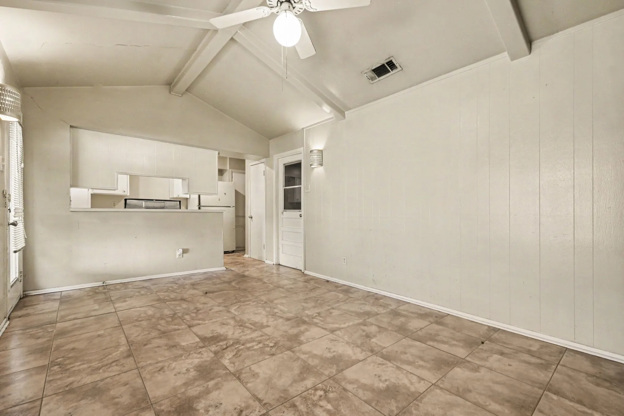 Vaulted ceiling with exposed beams, ceiling fan light fixture, tile flooring, and paneled walls