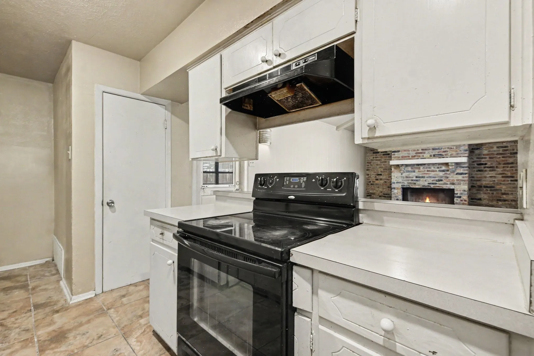 White cabinetry with matching hardware, black range with overhead ventilation, light-toned countertops, and tile flooring