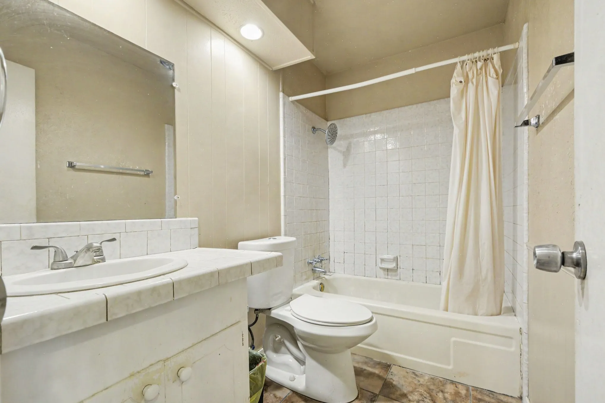 Bathroom featuring a built-in vanity with tiled countertop, an integrated sink with chrome faucet, a wall-mounted mirror, and a shower-over-tub with tiled surround