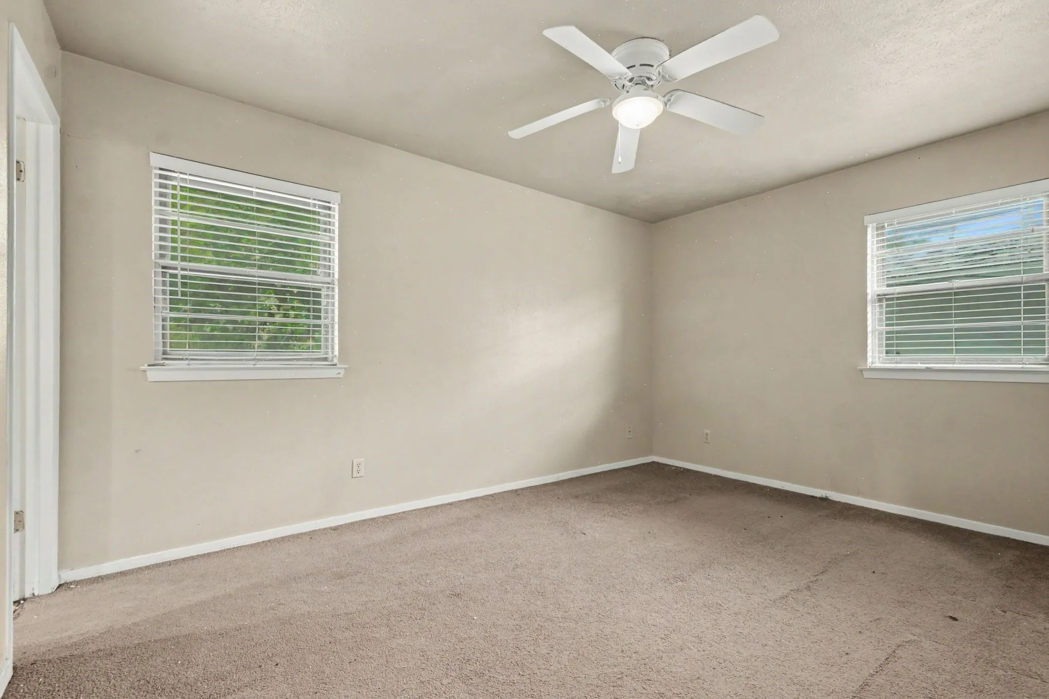 Neutral paint palette, ceiling fan with integrated lighting, two windows with blinds, and carpeted flooring
