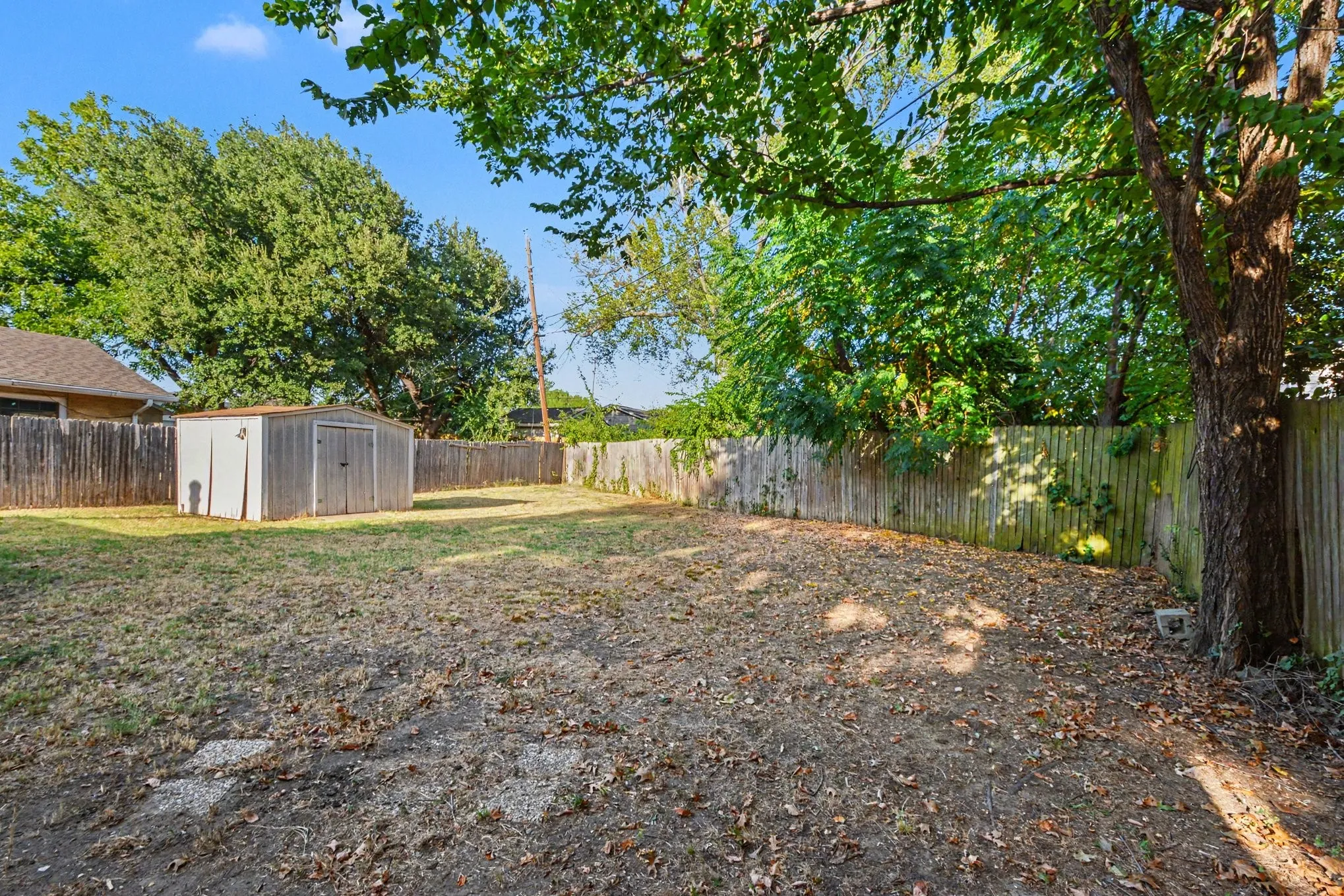 Fenced backyard featuring mature trees, a storage shed, and a privacy fence