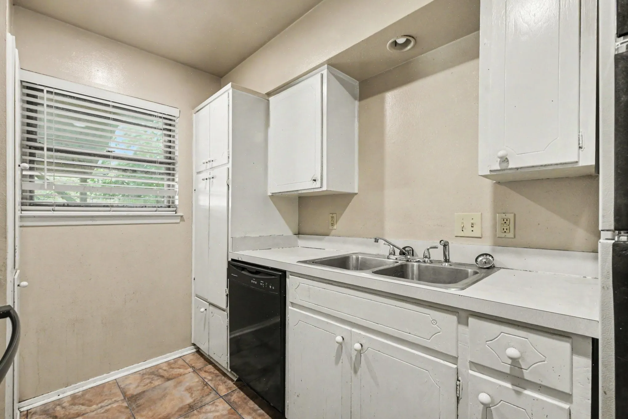 Kitchen featuring white cabinetry, a double basin stainless steel sink, black dishwasher, and tiled flooring