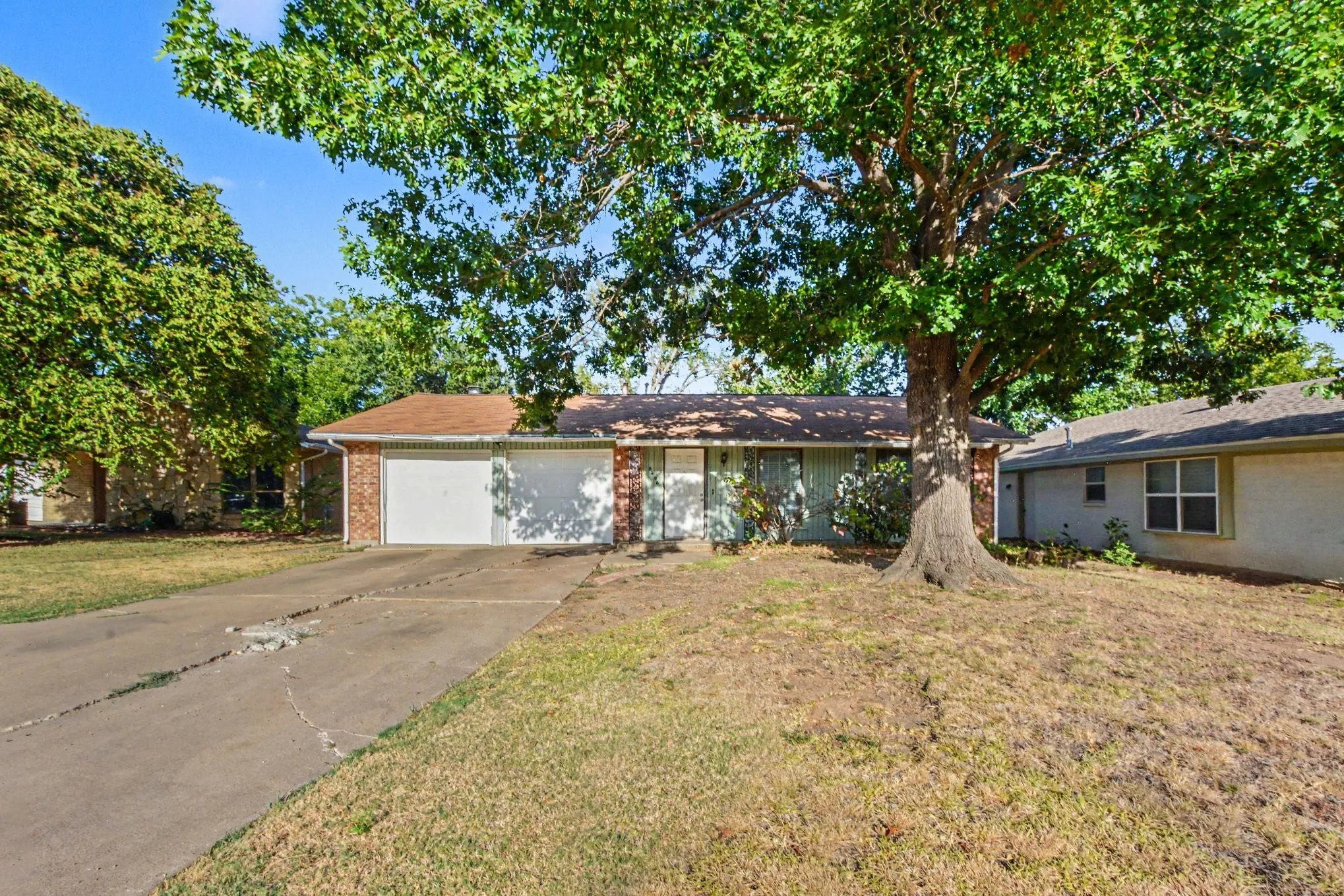 Brick facade exterior with a two-car garage, mature front yard tree, and an attached carport
