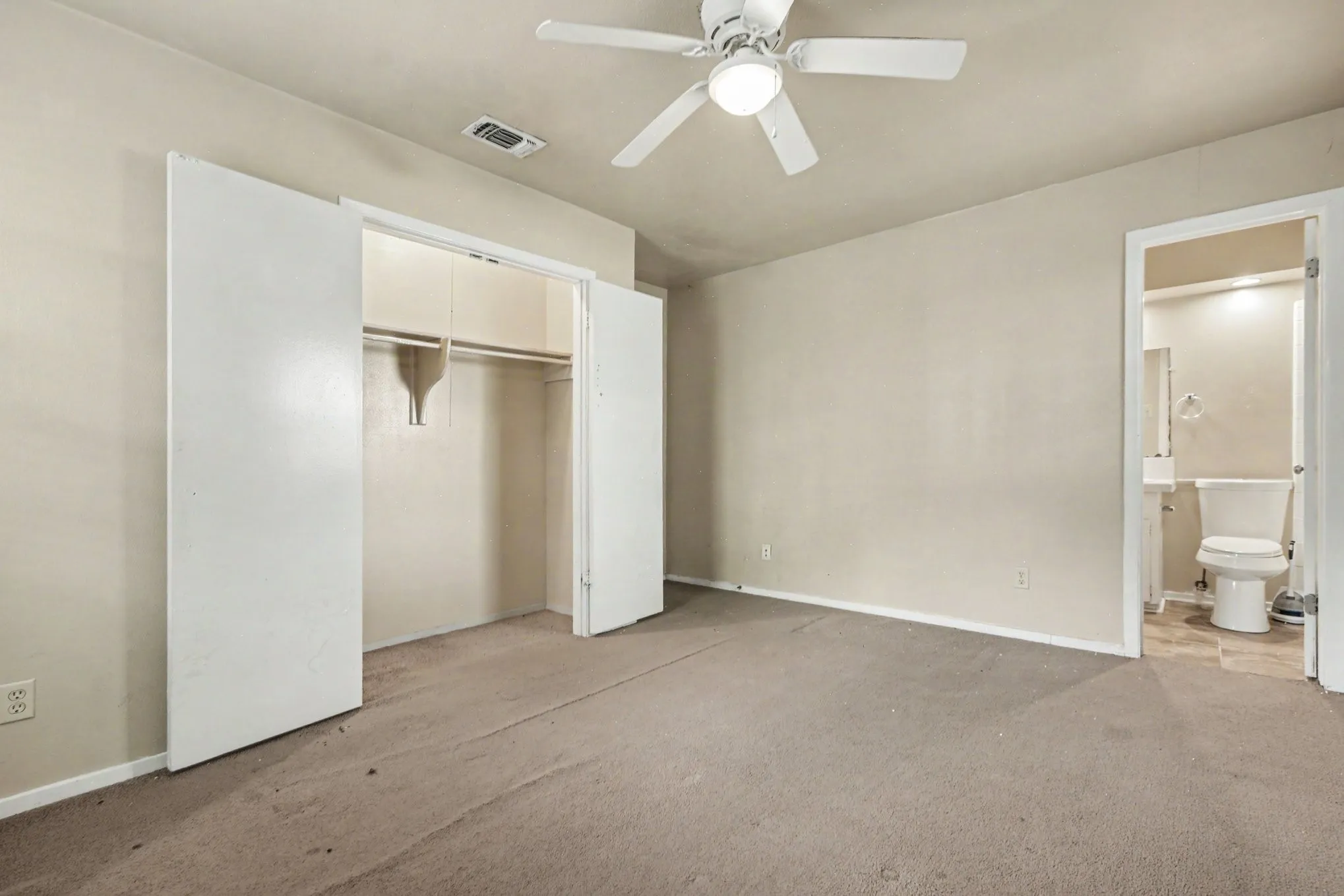 Carpeted room featuring a ceiling fan with integrated lighting, a spacious closet with bi-fold doors, and an en-suite bathroom with a toilet and pedestal sink