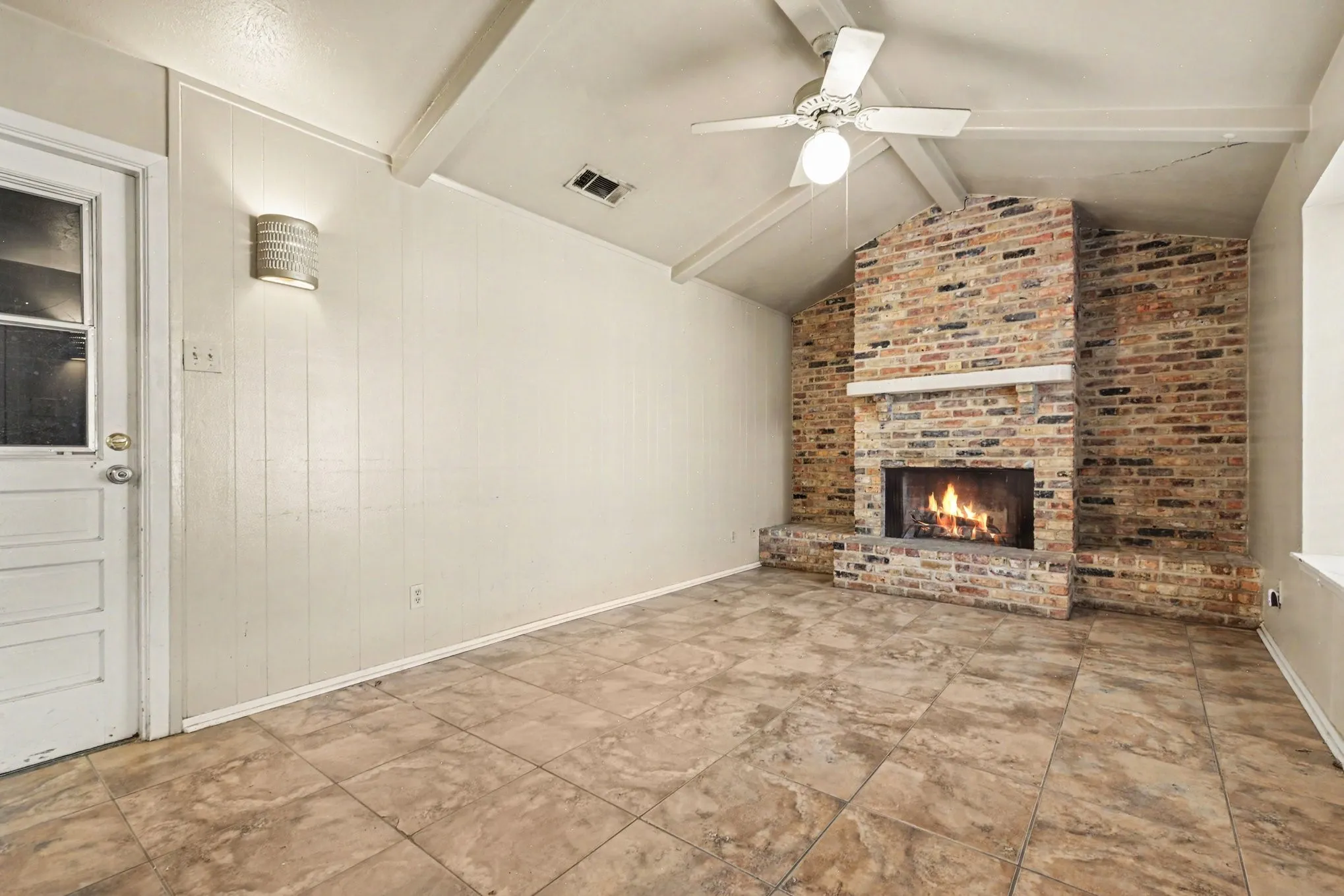 Brick fireplace with a stone mantel, vaulted ceiling with exposed beams, ceiling fan, and tile flooring