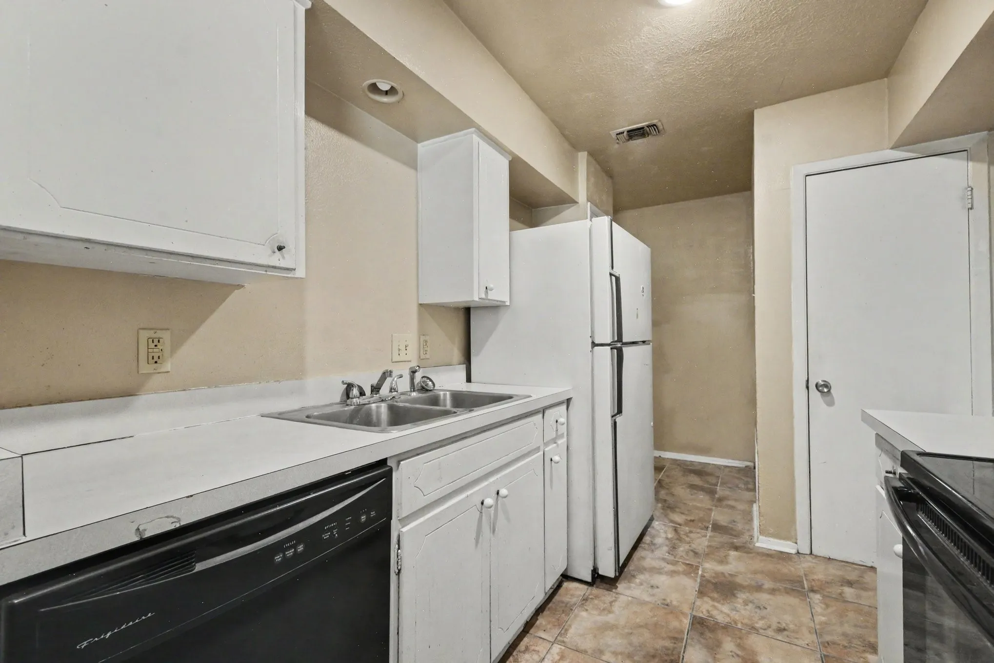 Kitchen featuring white cabinetry, a double basin stainless steel sink, a black dishwasher, a white refrigerator, and tile flooring