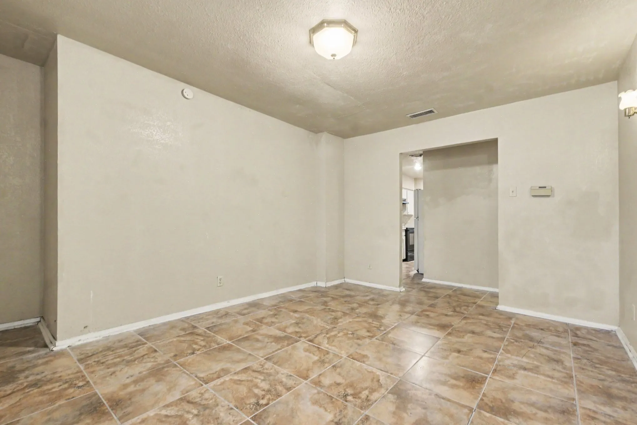 Spacious room featuring neutral wall tones, square tile flooring, a flush-mount ceiling light, and wall sconces