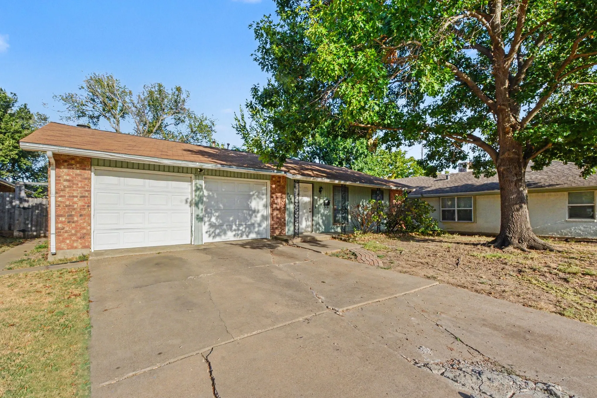 Front exterior featuring a two-car garage, brick facade accents, and mature shade trees