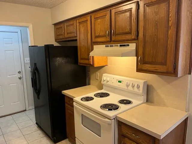 Kitchen featuring wood-finish cabinetry, light-toned countertops, a black refrigerator, and a white electric range
