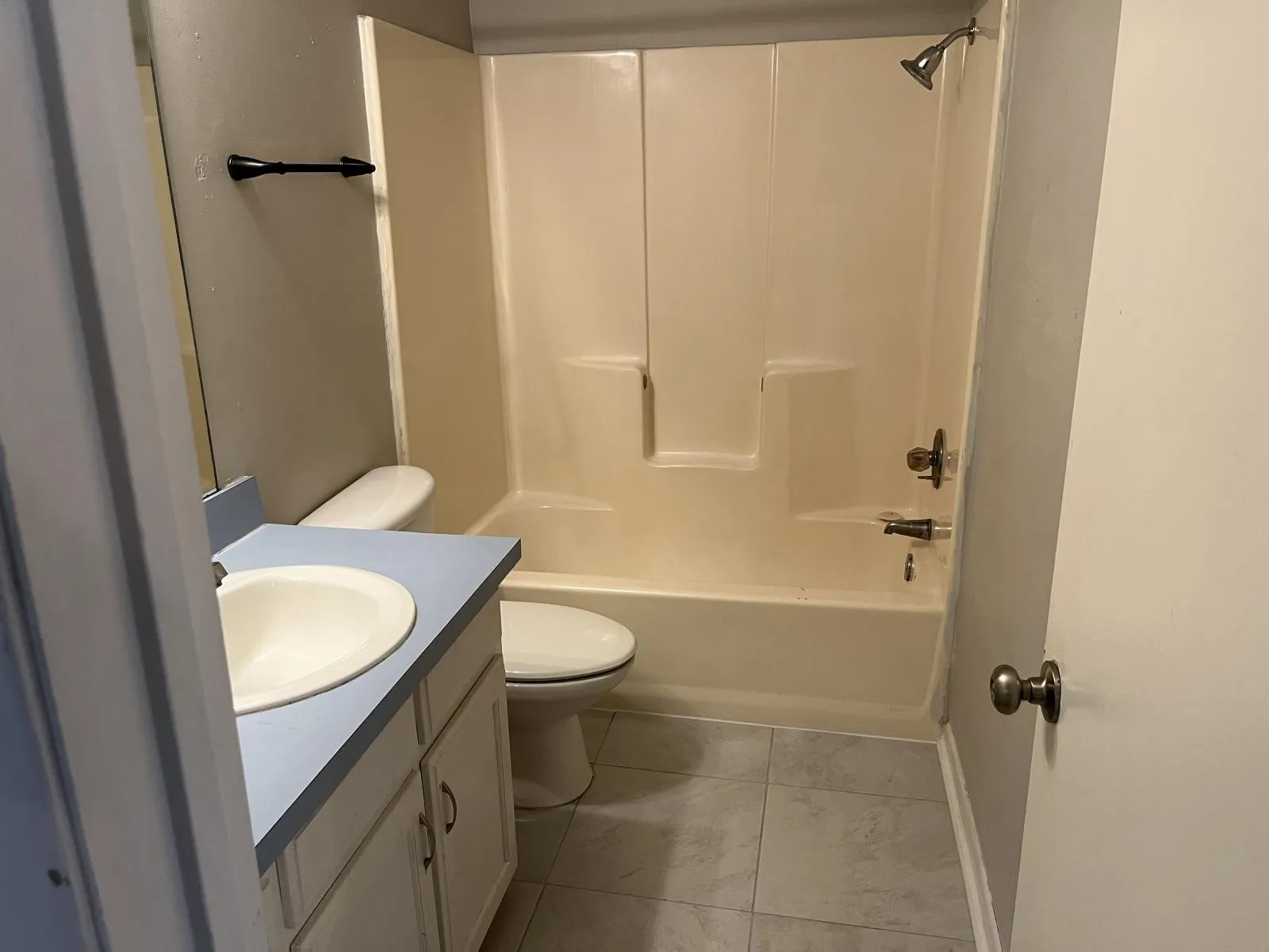 Bathroom featuring a light-colored vanity with an integrated sink and light blue countertop, a toilet, a shower/tub combination with a showerhead, and tiled flooring