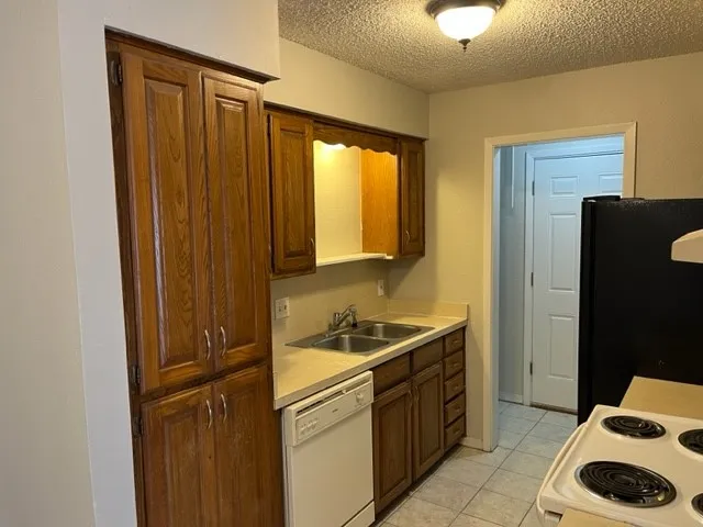 Kitchen featuring wood cabinetry, a double basin stainless steel sink, tile flooring, and a built-in dishwasher