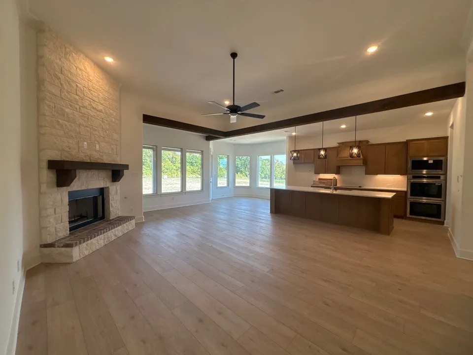 Open concept living space featuring a stone fireplace, wood-finish flooring, exposed ceiling beams, a kitchen island, and built-in stainless steel appliances